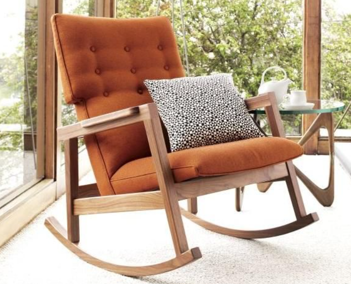 A rocking chair with orange cushions and a pillow, also known as a nursing chair.